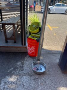 An orange home depot bucket holding a yellow fan outside.