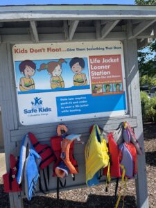 An image of multicolored life jackets with a sign about child swimming safety. 